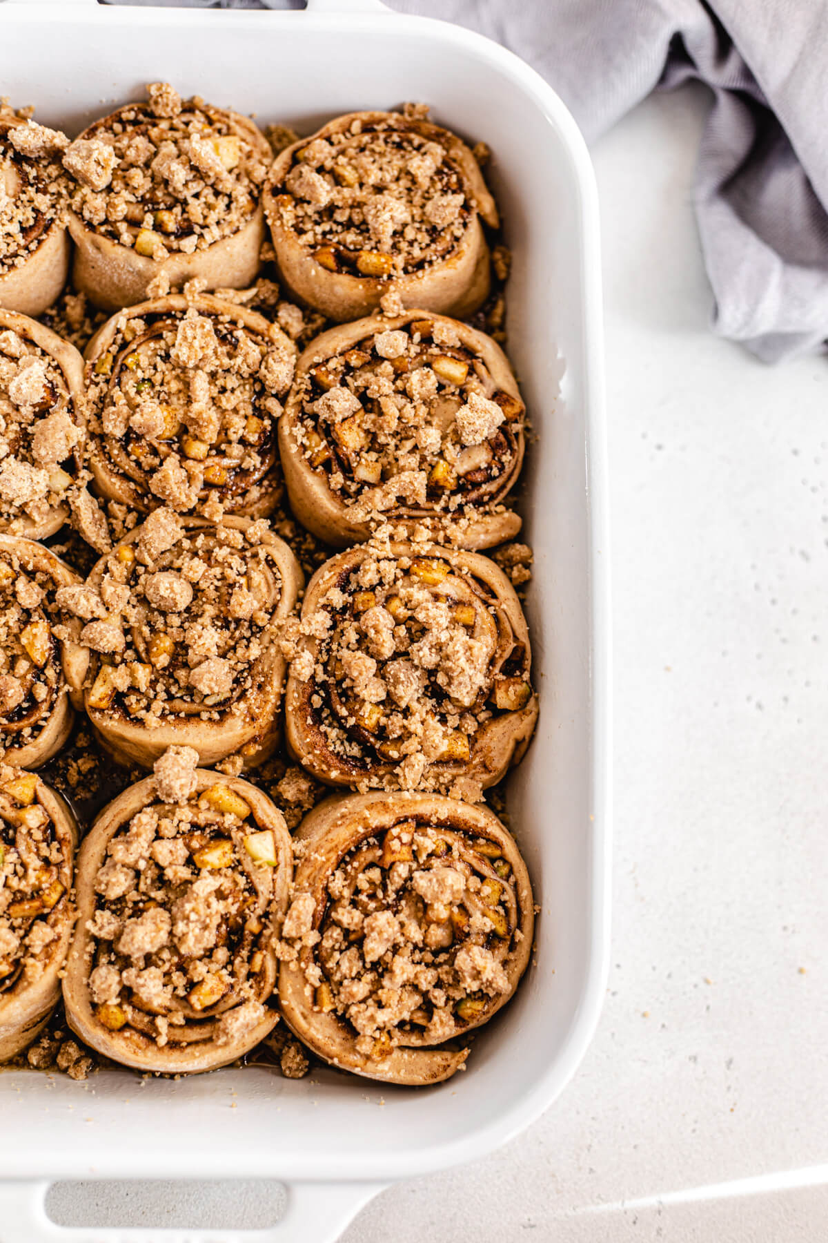 unbaked cinnamon rolls topped with crumble in a white baking dish