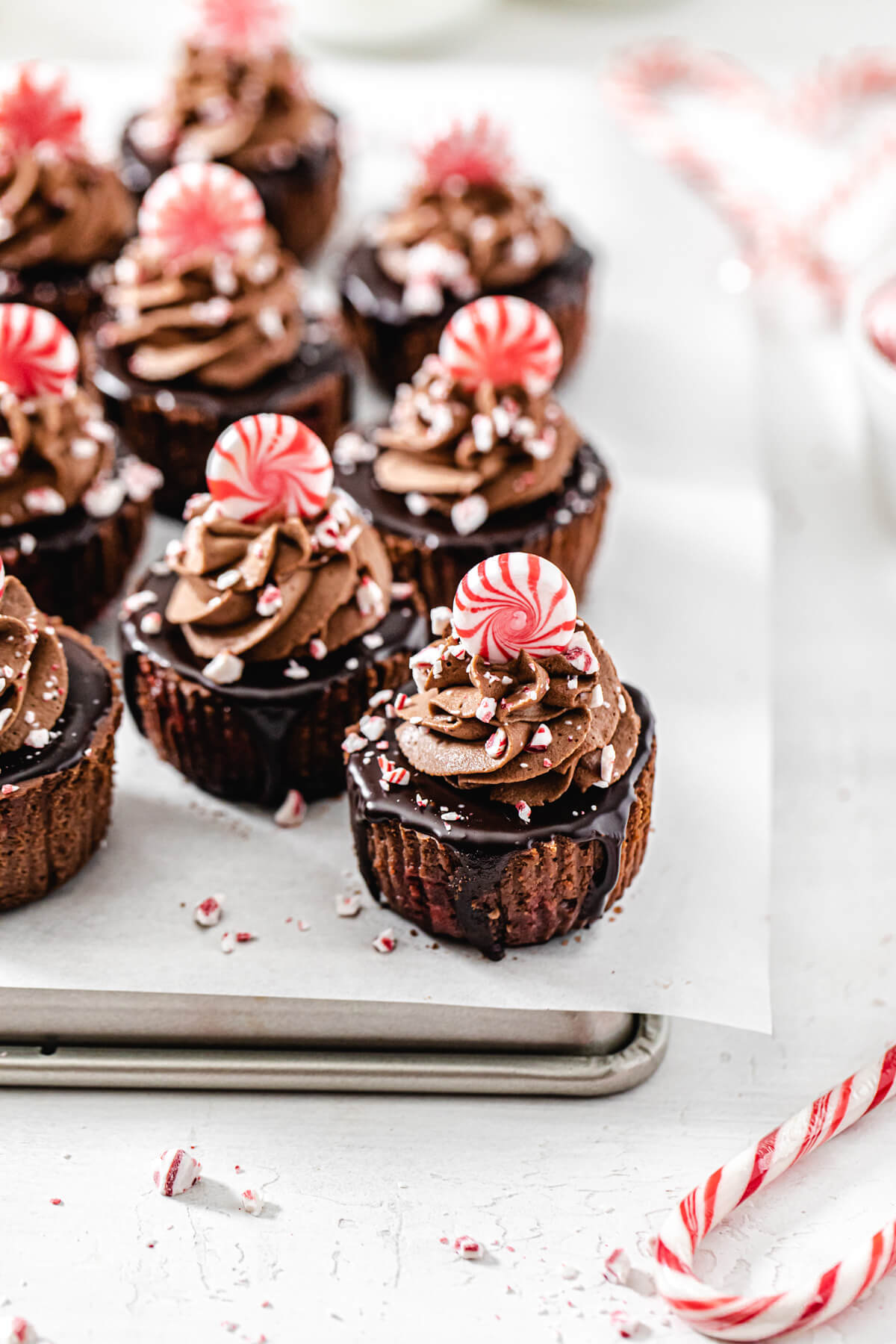 angled view of mini cheesecakes on a parchment lined baking sheet with a candy cane in front