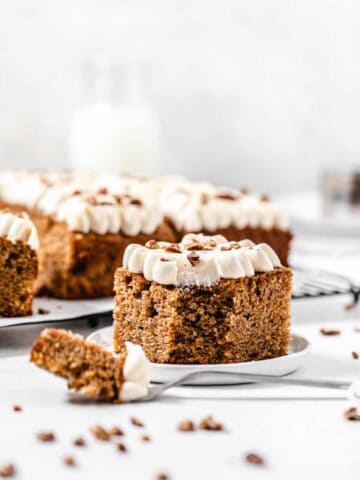 slice of carrot sheet cake on a small white plate with a fork in front of it and slices in the background