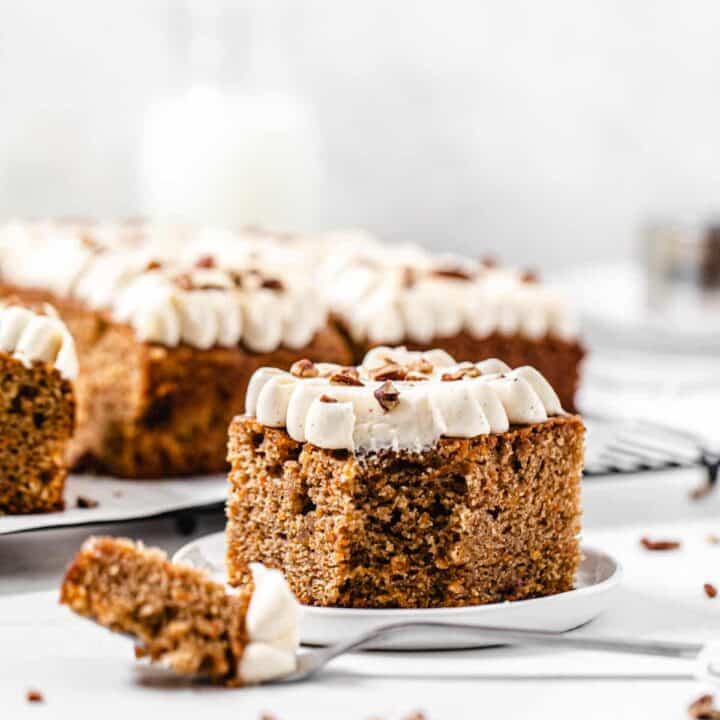 slice of carrot sheet cake on a small white plate with a fork in front of it and slices in the background