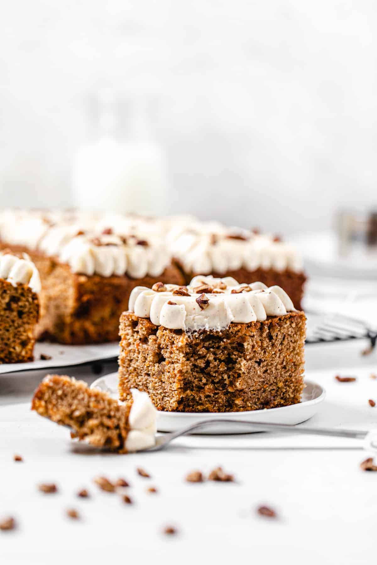 slice of carrot sheet cake on a small white plate with a fork in front of it and slices in the background