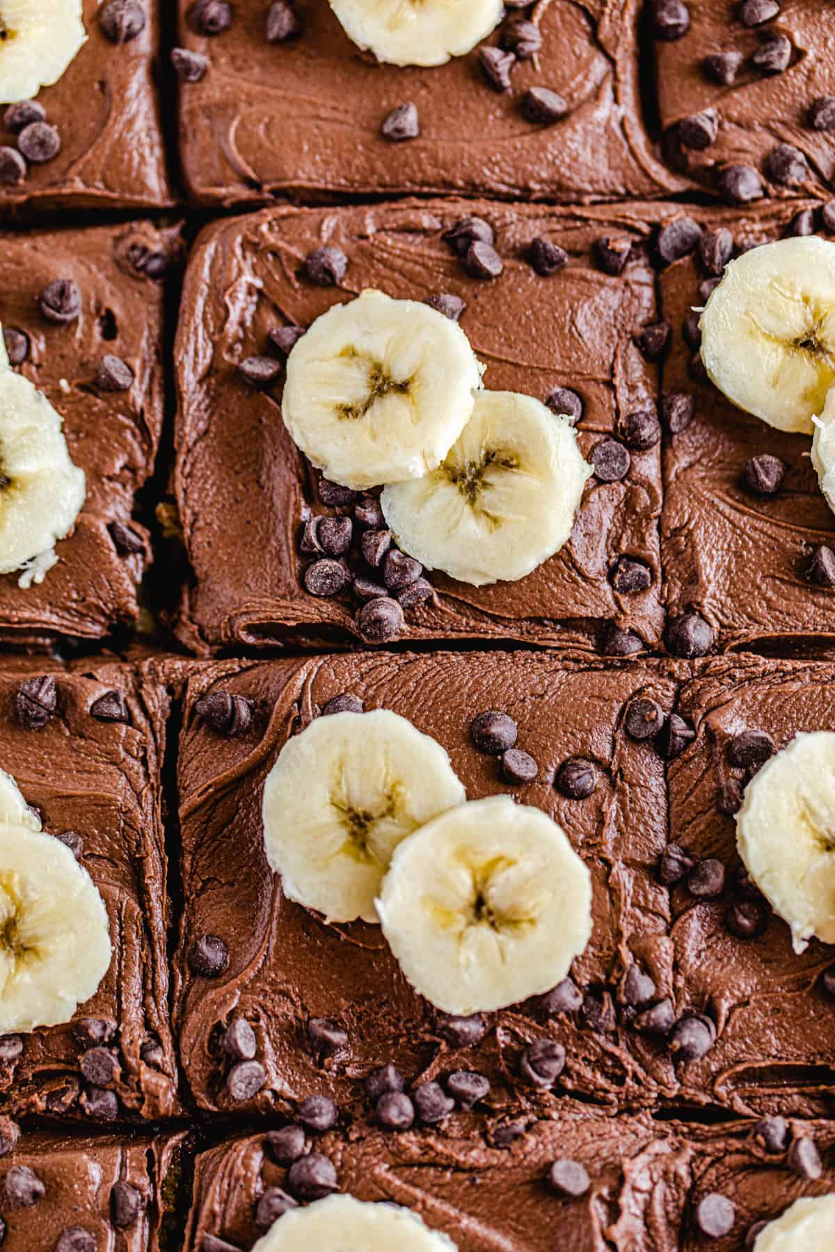 close up of cake topped with chocolate frosting, banana slices and mini chocolate chips