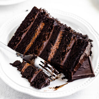 slice of chocolate cake on a white plate with fork taking a piece off