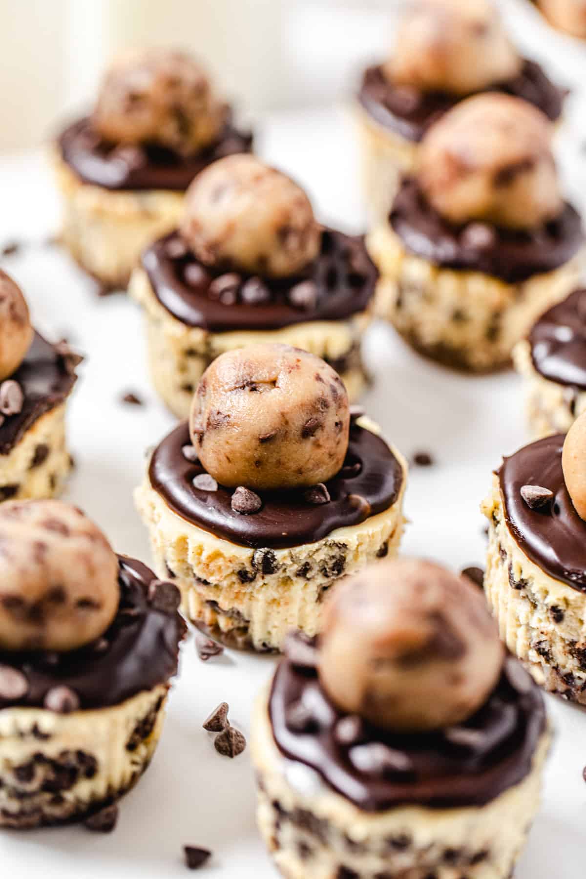 multiple mini cookie dough topped cheesecakes with mini chocolate chips scattered around them