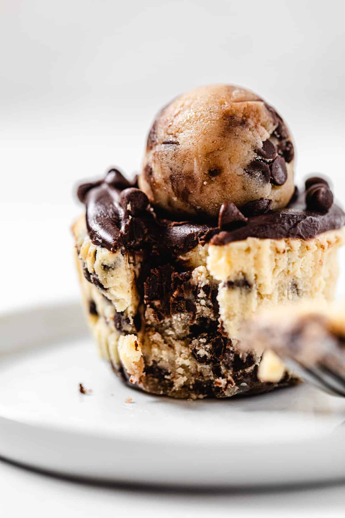 close up of a cheesecake cupcake on a small white plate with a fork bite taken out of it