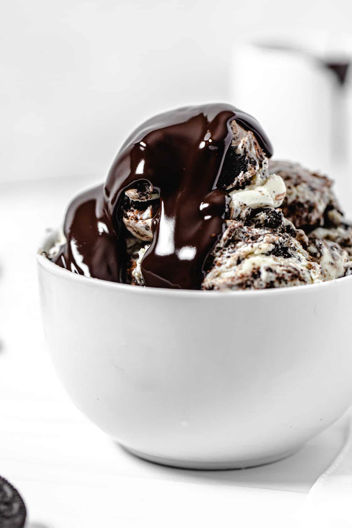 close up of ice cream in a white bowl topped with ganache
