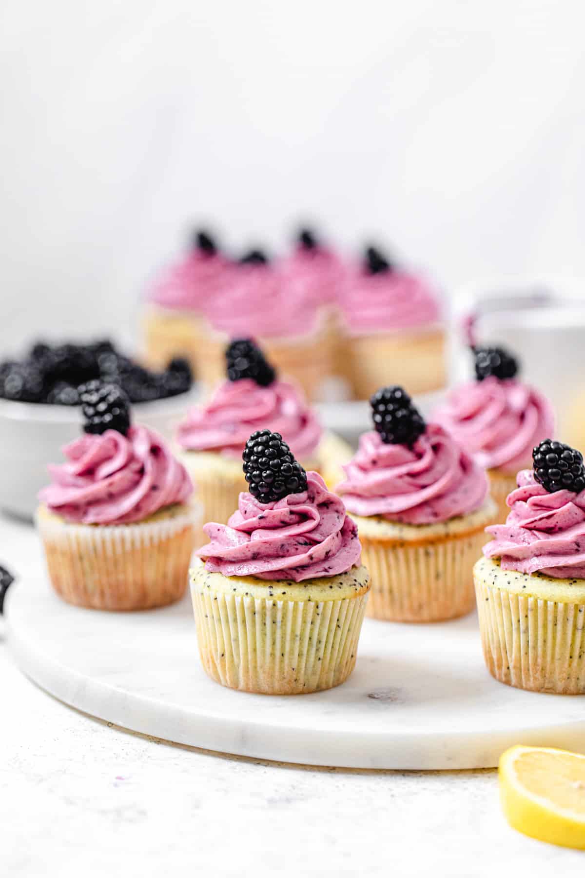 cupcakes on a round marble board with bowl of blackberries in the background