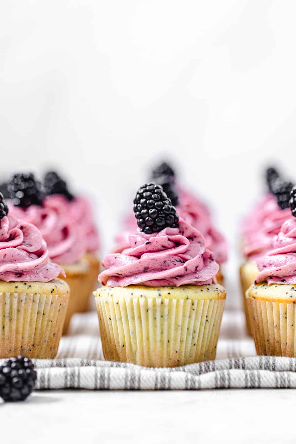 three rows of frosted cupcakes on a striped grey dish towel