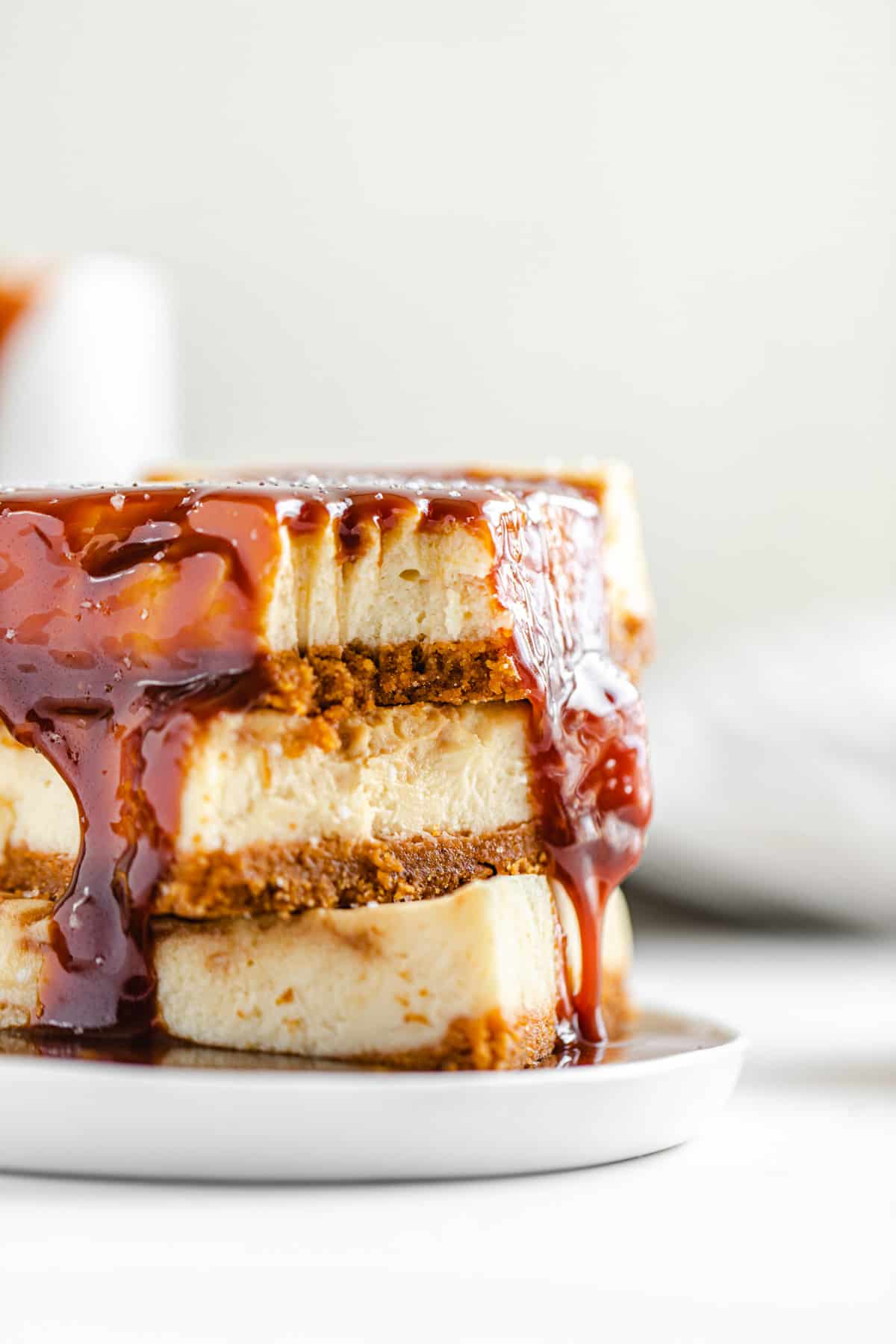 close up of cheesecake bar stack covered in caramel sauce on a white appetizer plate