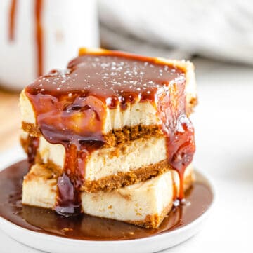 stack of cheesecake bars on a small white plate with caramel sauce poured on top of the stack