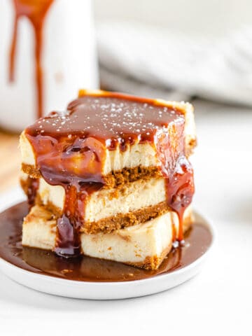 stack of cheesecake bars on a small white plate with caramel sauce poured on top of the stack