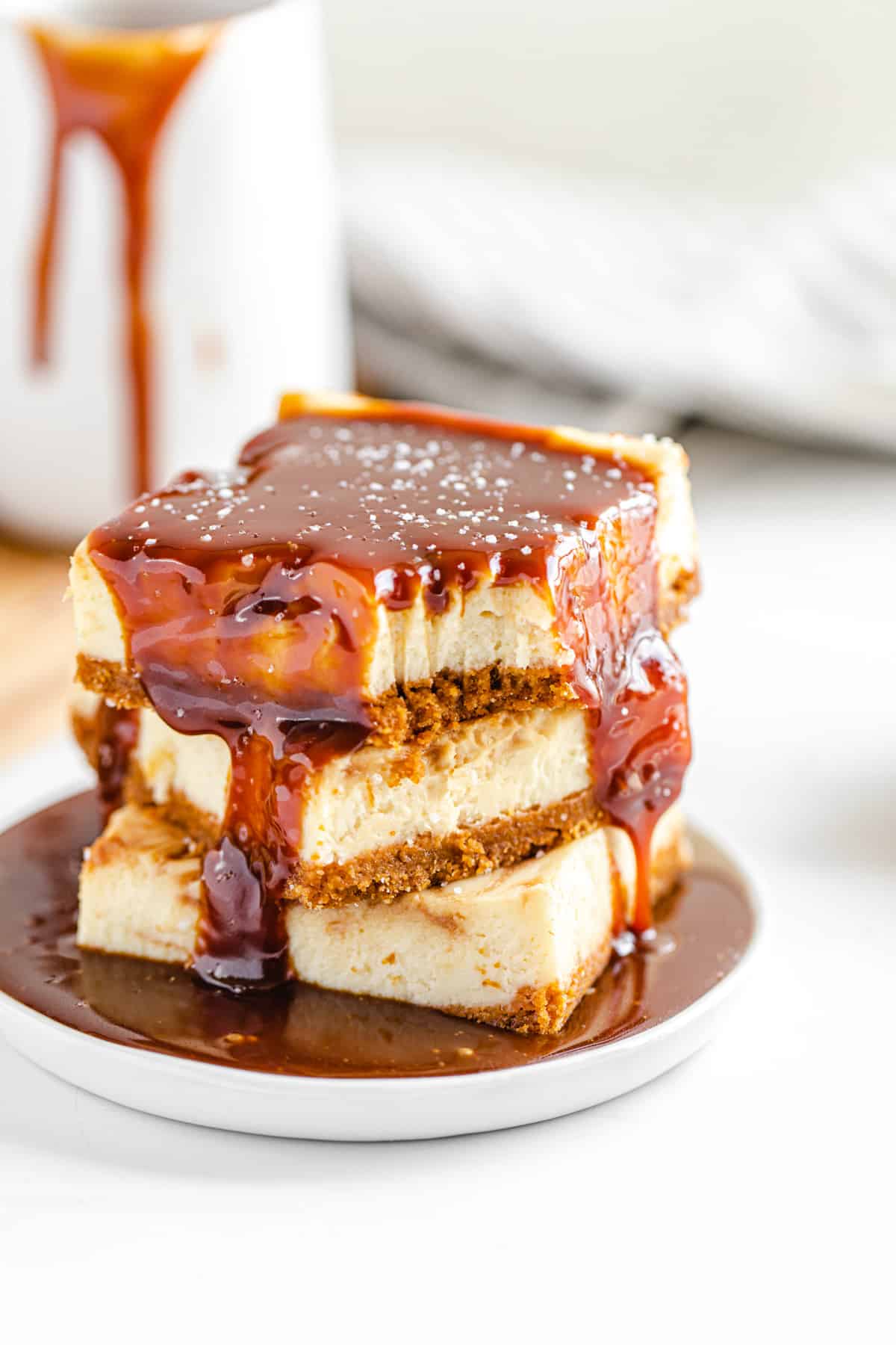 stack of cheesecake bars on a small white plate with caramel sauce poured on top of the stack