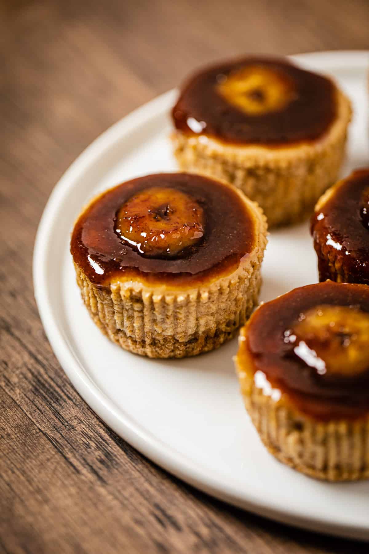 cheesecake cupcakes topped with bananas foster sauce on a white plate