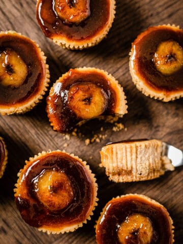 top view of small banana cheesecakes topped with bananas foster. The middle cheesecake has a fork bite taken out of it.