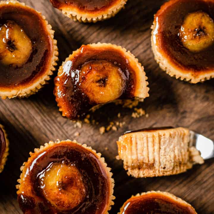 top view of small banana cheesecakes topped with bananas foster. The middle cheesecake has a fork bite taken out of it.