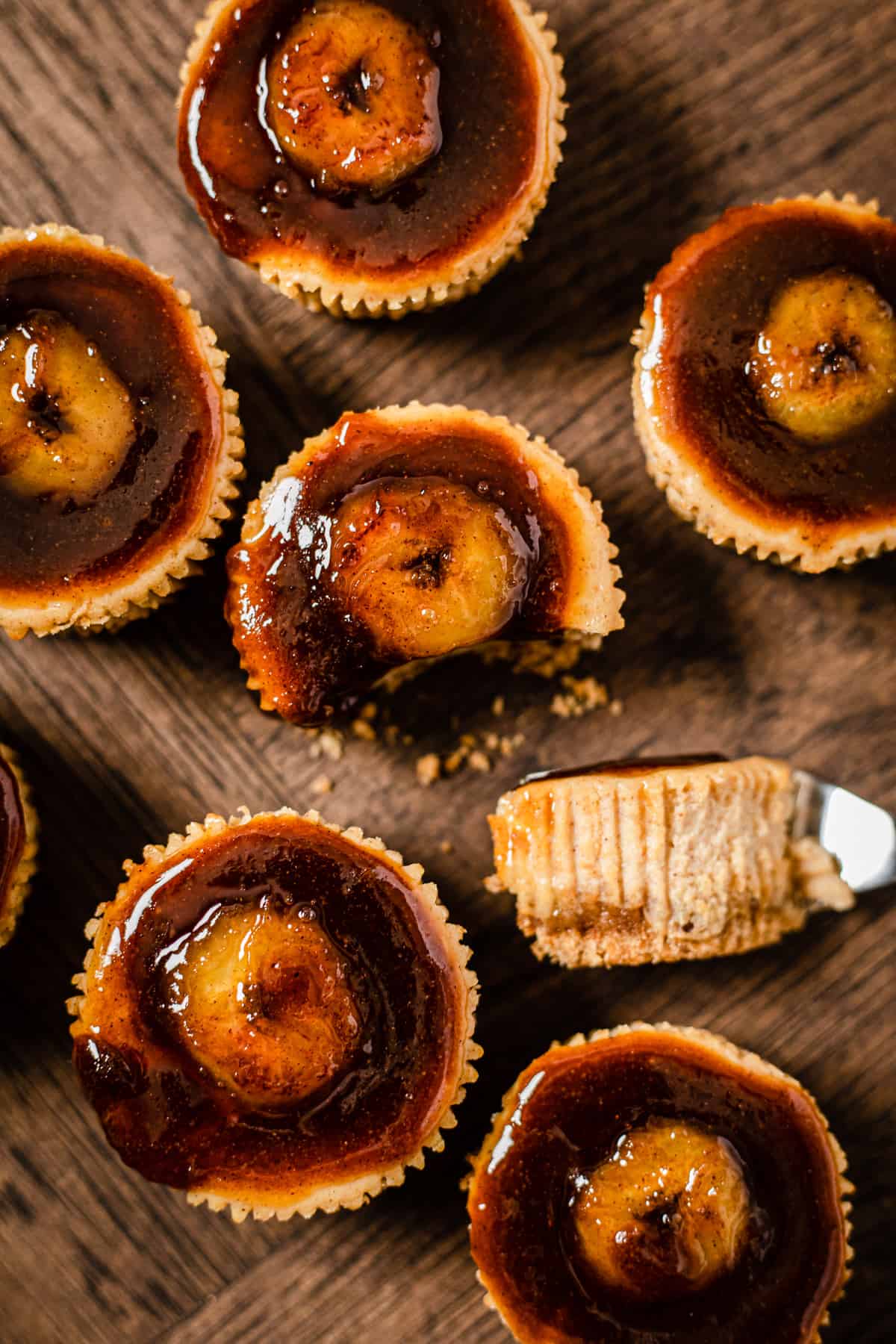 top view of small banana cheesecakes topped with bananas foster. The middle cheesecake has a fork bite taken out of it.