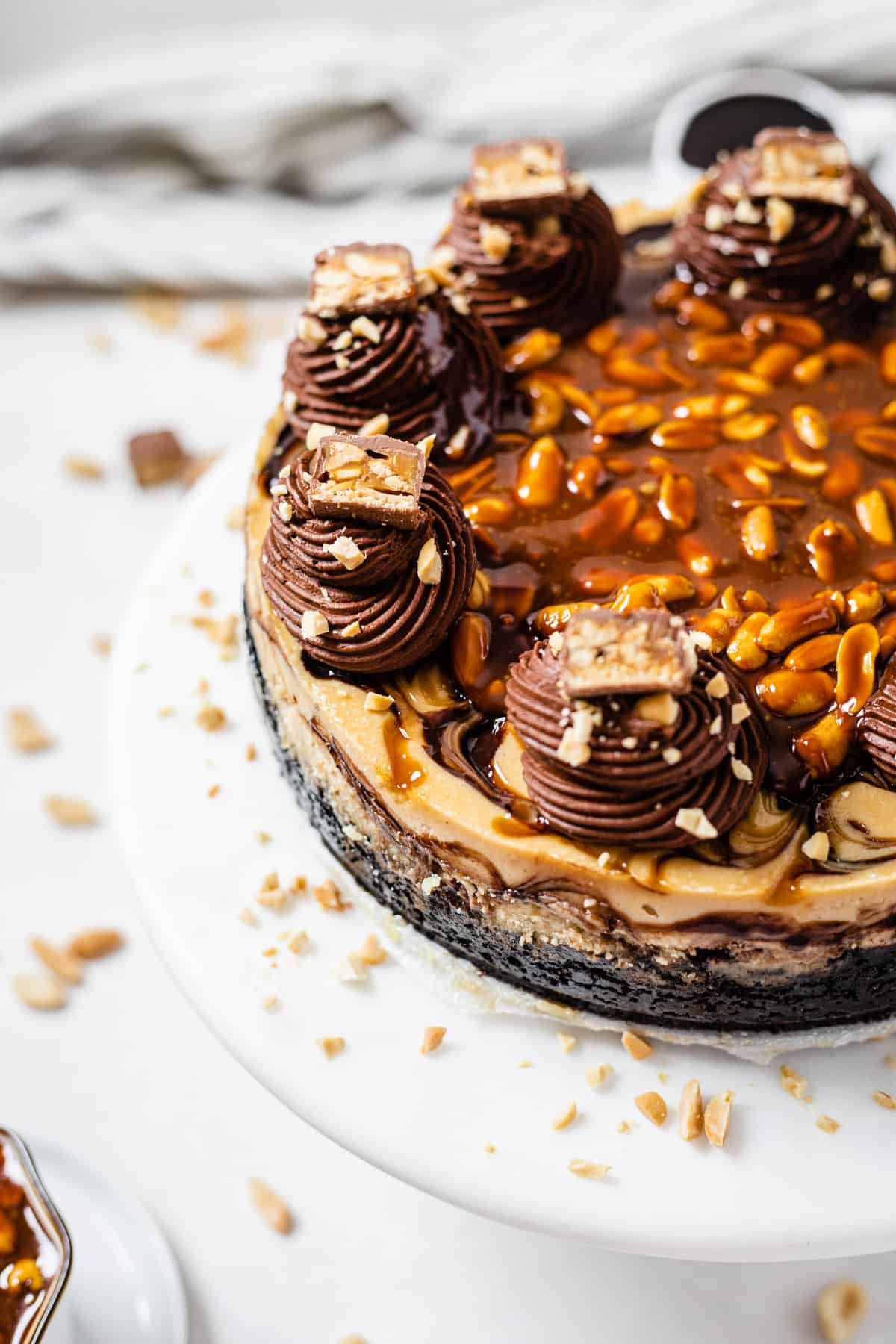 whole cheesecake on a cake stand with chopped peanuts scattered around it