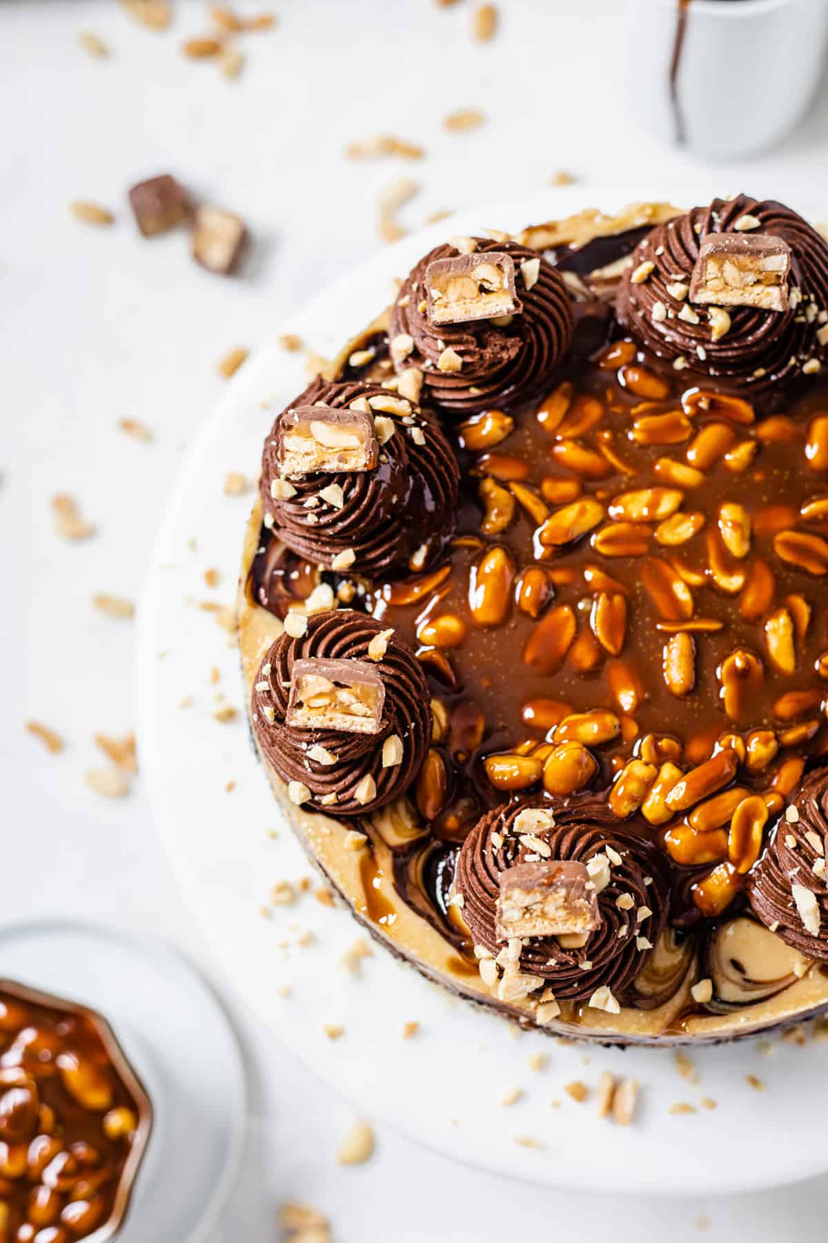 top view of cheesecake on a cake stand with caramel peanut sauce in a white dish on the bottom left