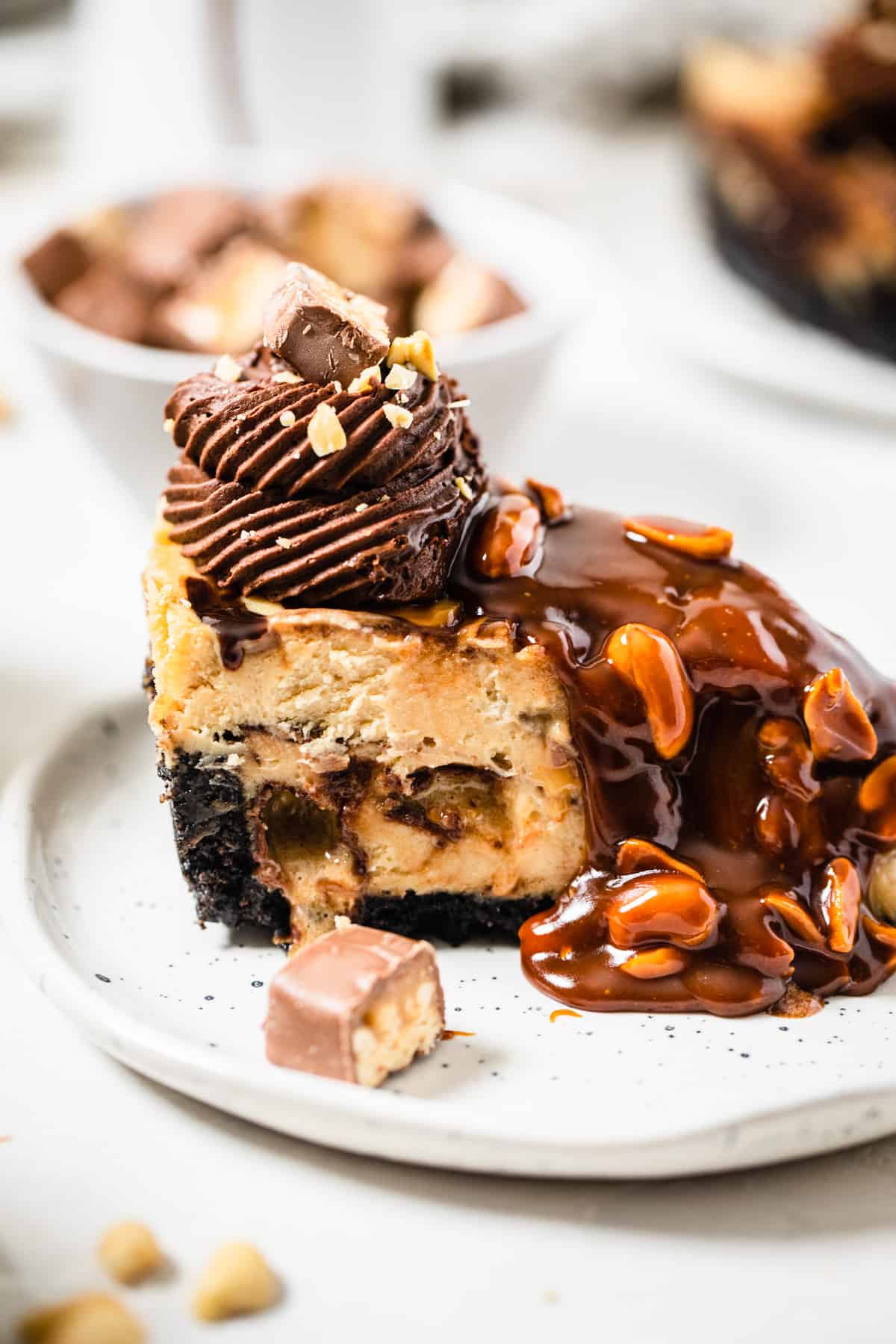 sideview of snickers stuffed cheesecake on a small white plate