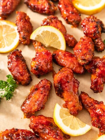 hot chicken wings, lemon slices and parsley on a brown sheet of parchment paper