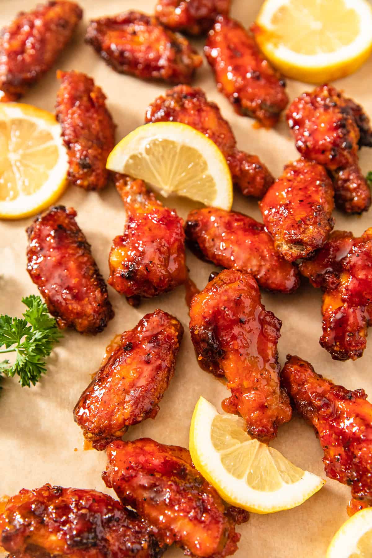 hot chicken wings, lemon slices and parsley on a brown sheet of parchment paper