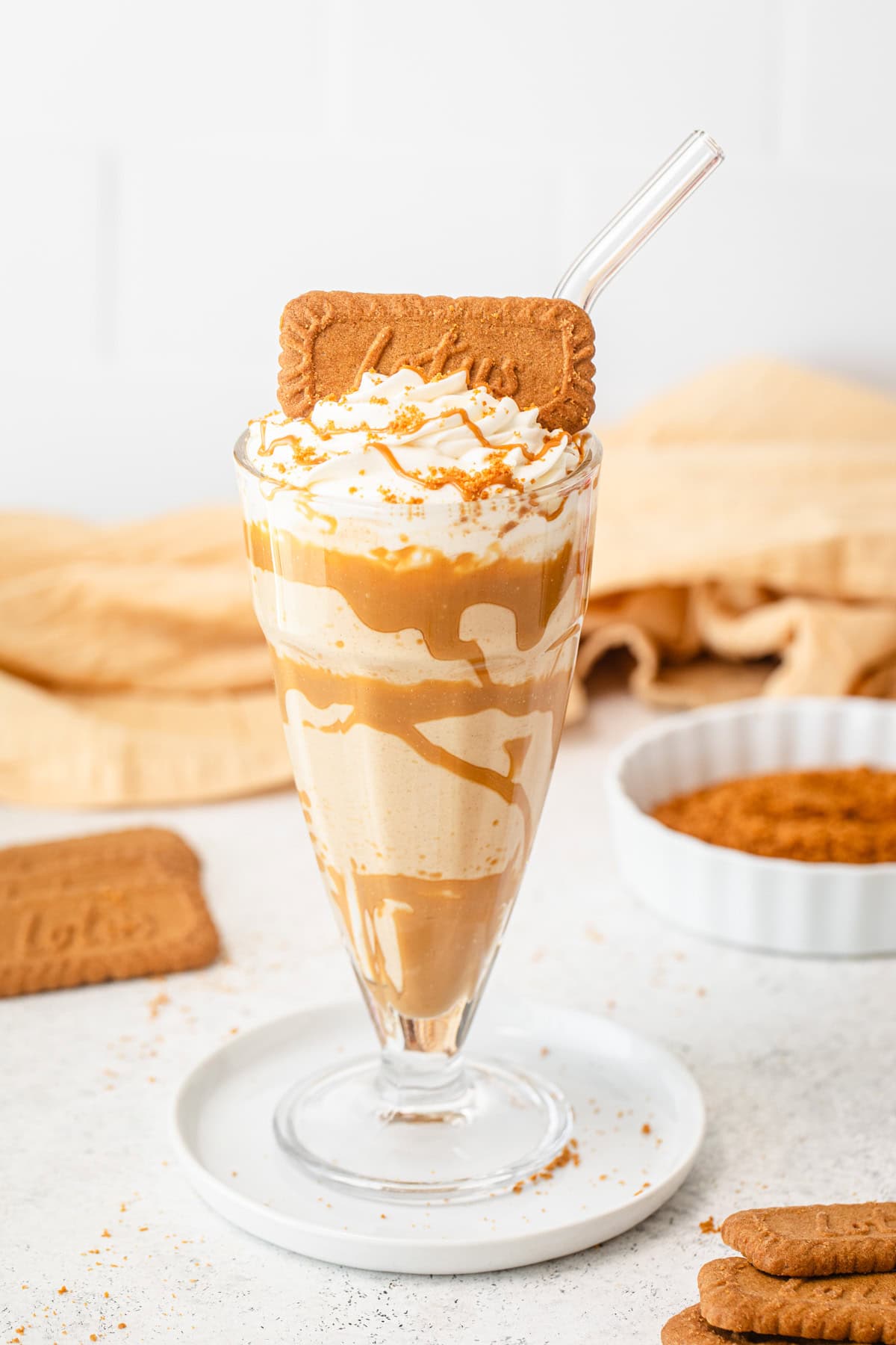 One milkshake on a small plate with cookies and a cloth behind it