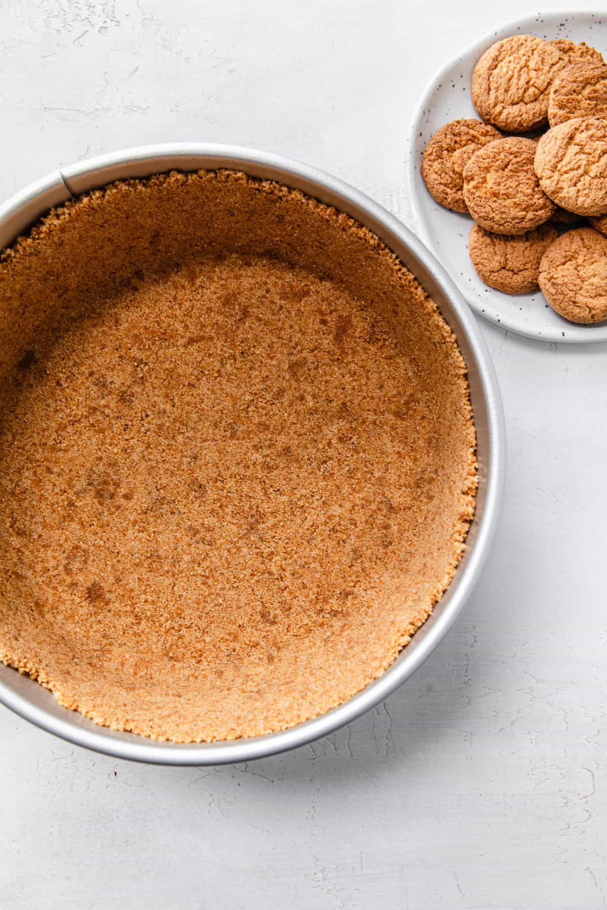 coconut cookie crust in a springform pan with a plate of coconut cookies on the side