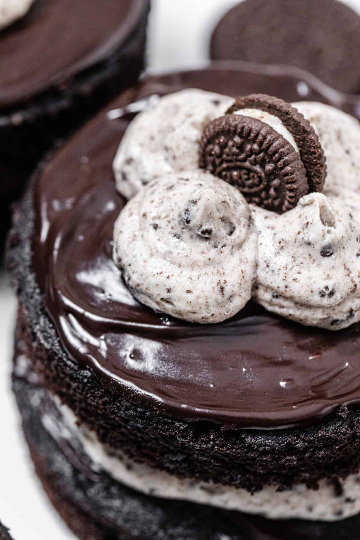 top of mini chocolate layer cake topped with ganache cookies and cream frosting poofs and mini chocolate cookie sandwich
