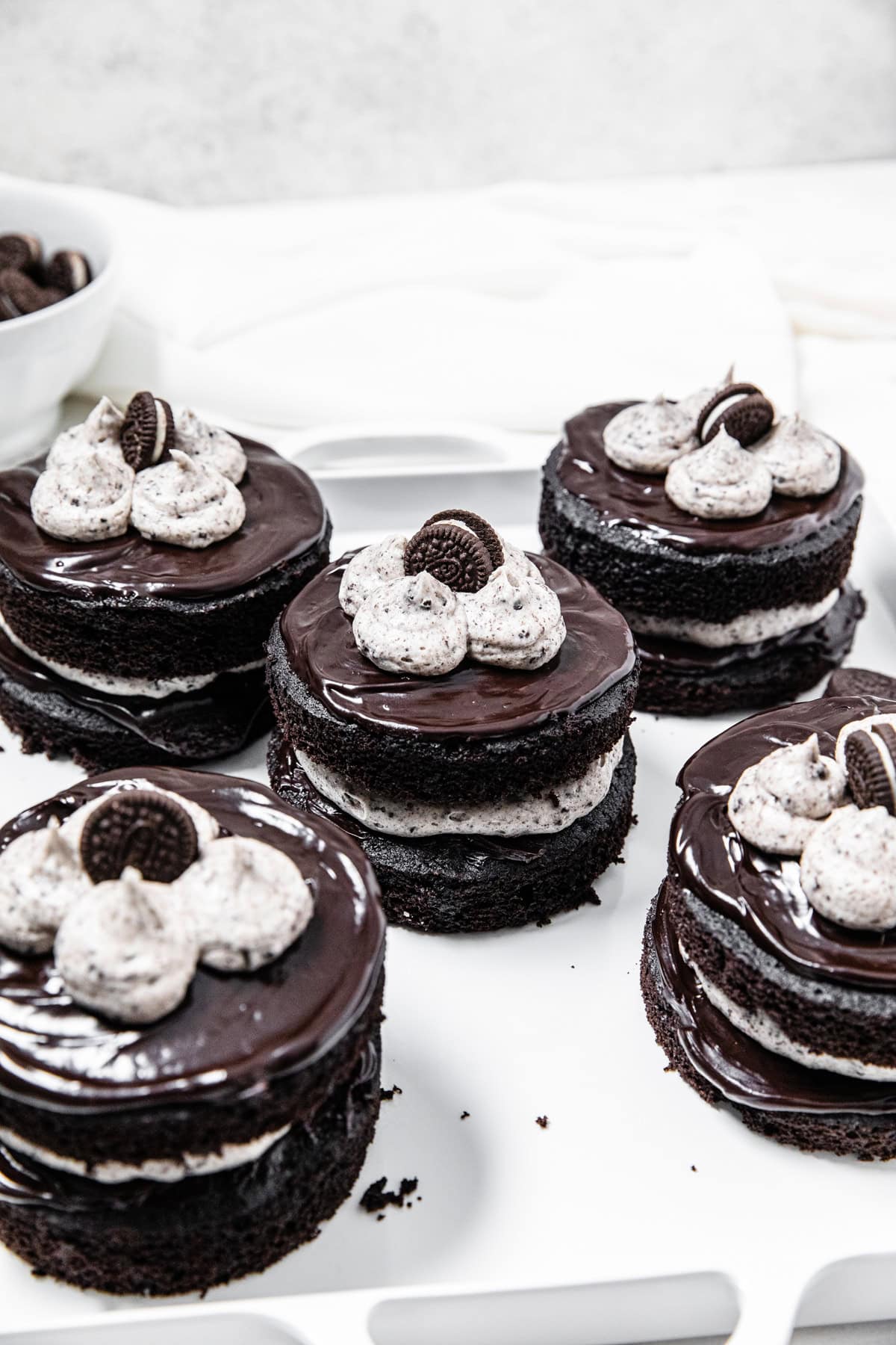 Mini chocolate cookies and cream cakes layered with chocolate ganache, cookies and cream frosting and mini chocolate sandwich cookies on a white serving platter