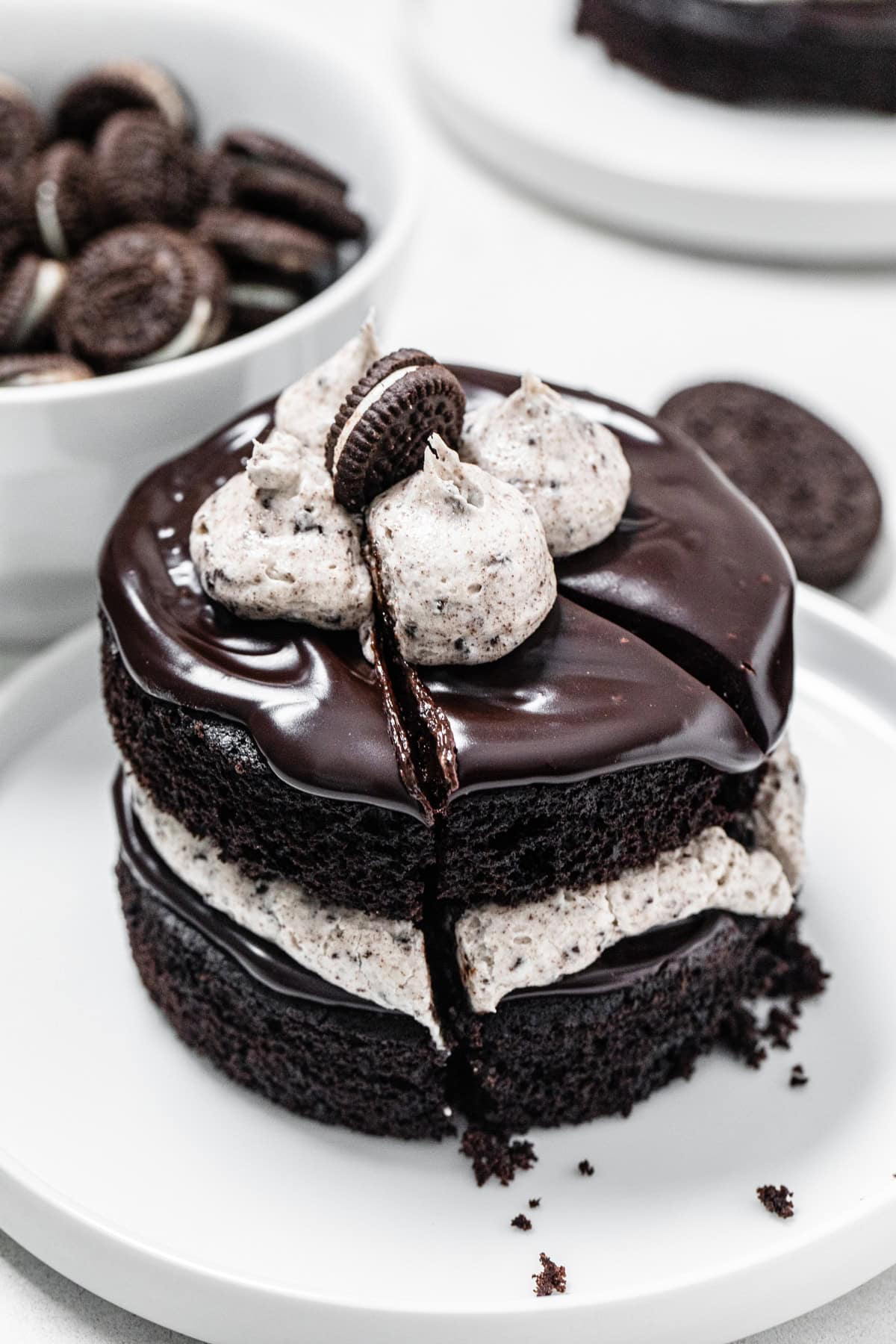 individual sized chocolate cookies and cream cake with a piece sliced, arranged on a small white plate with a bowl of mini Oreos in the background